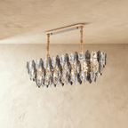 Clérachic oval chandelier of tiered smoked and clear crystal leaves, hung from a gold bar canopy on wrapped cords, against limewash.