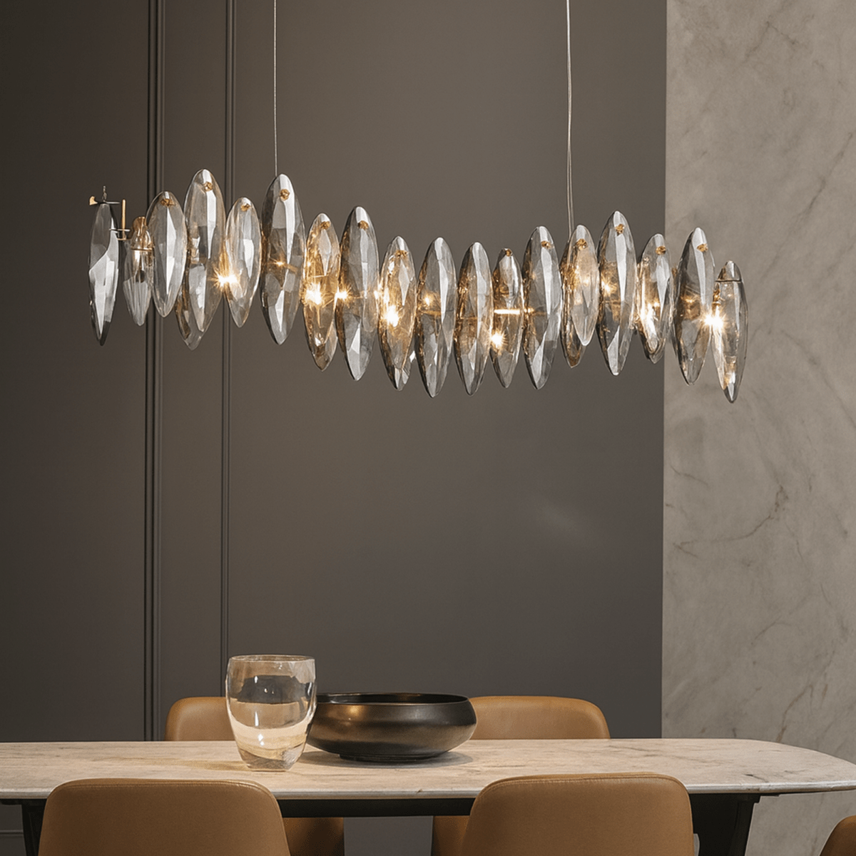 Clérachic long wave chandelier of smoked crystal leaves above a marble dining table with tan leather chairs and a dark bowl.