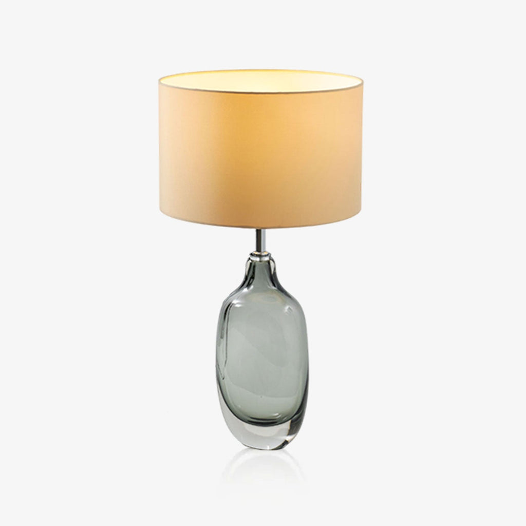 A Clérachic table lamp with a smoky grey glass base and a cream drum shade, lit warmly against a plain white backdrop.