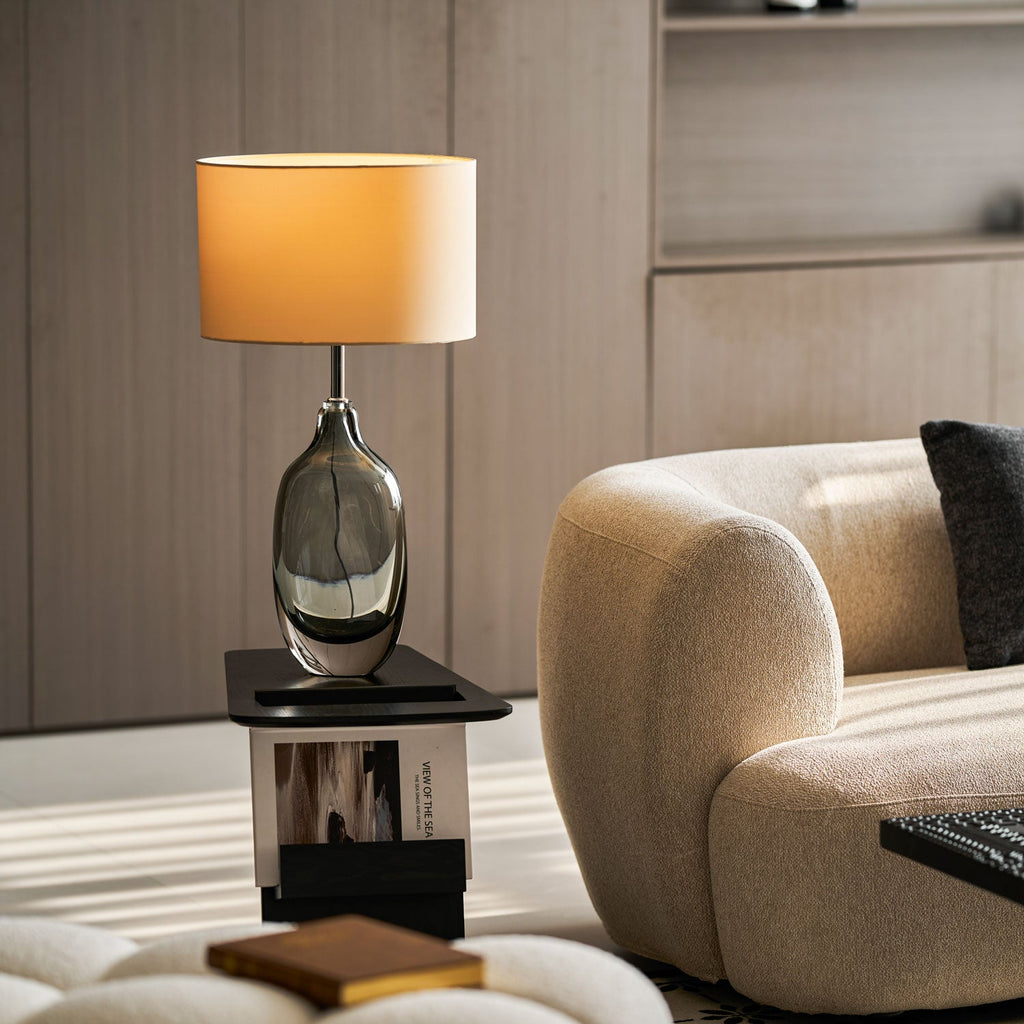 The Clérachic table lamp glowing on a black side table above a stacked book, beside a curved cream boucle sofa.