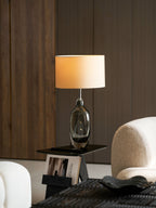 Seen in a quieter corner, this Clérachic lamp glows above a black side table, with a cream armchair beside it and a dark tray below.
