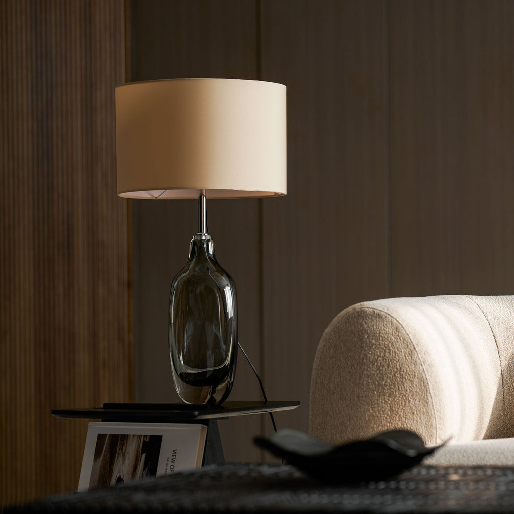Switched off, this Clérachic table lamp shows a pale cream shade and a grey glass base, with a low tray in the foreground.