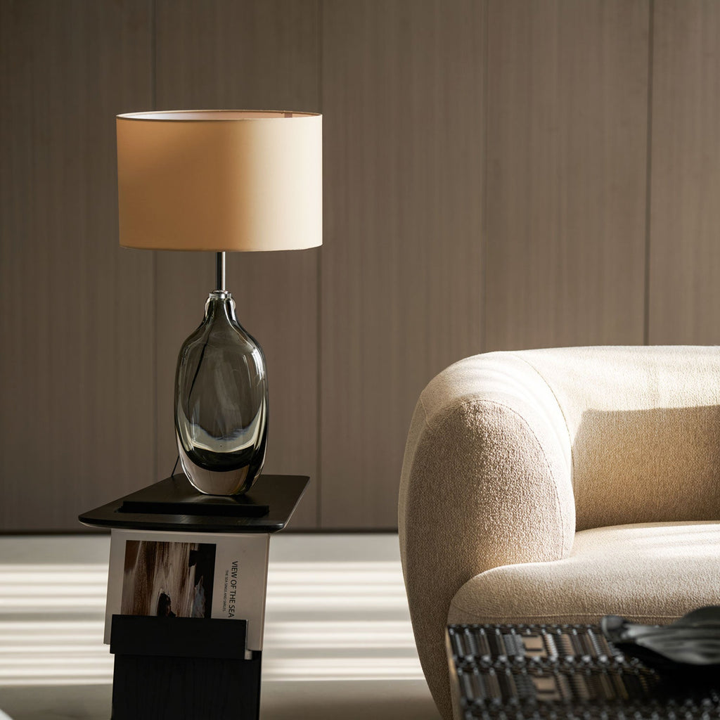 The Clérachic table lamp unlit on a dark side table, its cream shade catching daylight beside a rounded cream sofa.