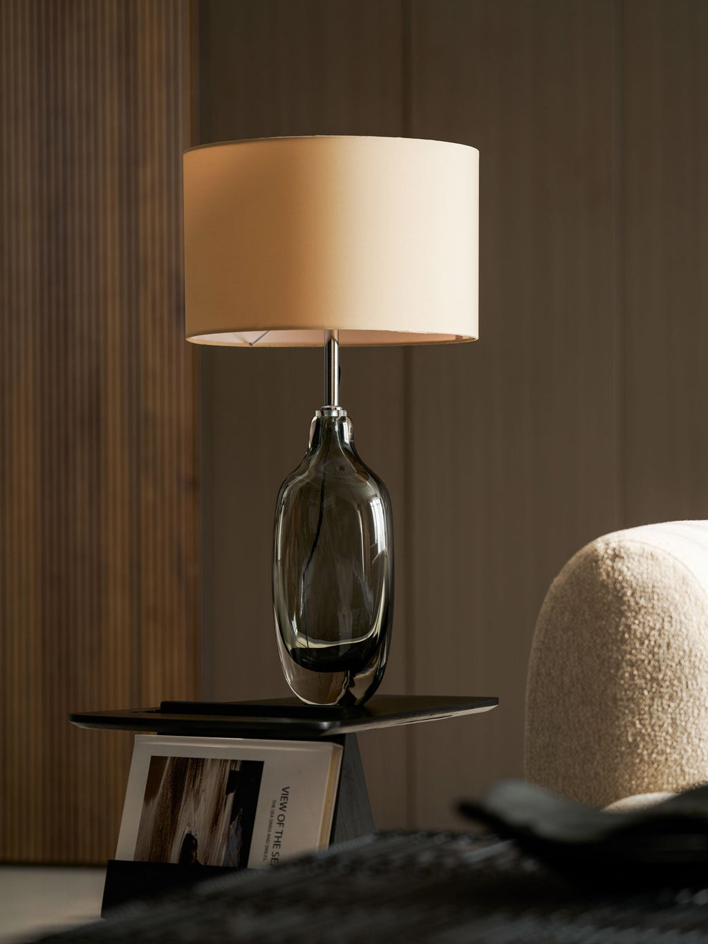Close view of the smoky glass base and slim metal neck of this Clérachic table lamp, with its cream shade above.