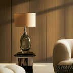 Warm side light falls across this Clérachic table lamp on a black stand, with a cream boucle armchair and a wood-slat wall.