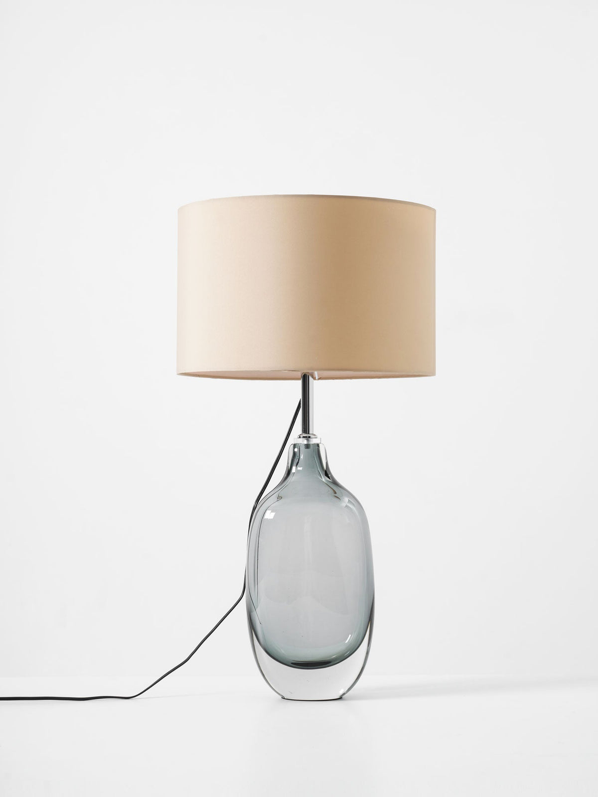 Front view of the Clérachic table lamp unlit on white, its grey glass base with a thick clear foot and its cord running off left.