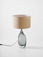 A three-quarter angle on the unlit Clérachic table lamp, showing its smoky glass base and cream shade on a pale grey backdrop.