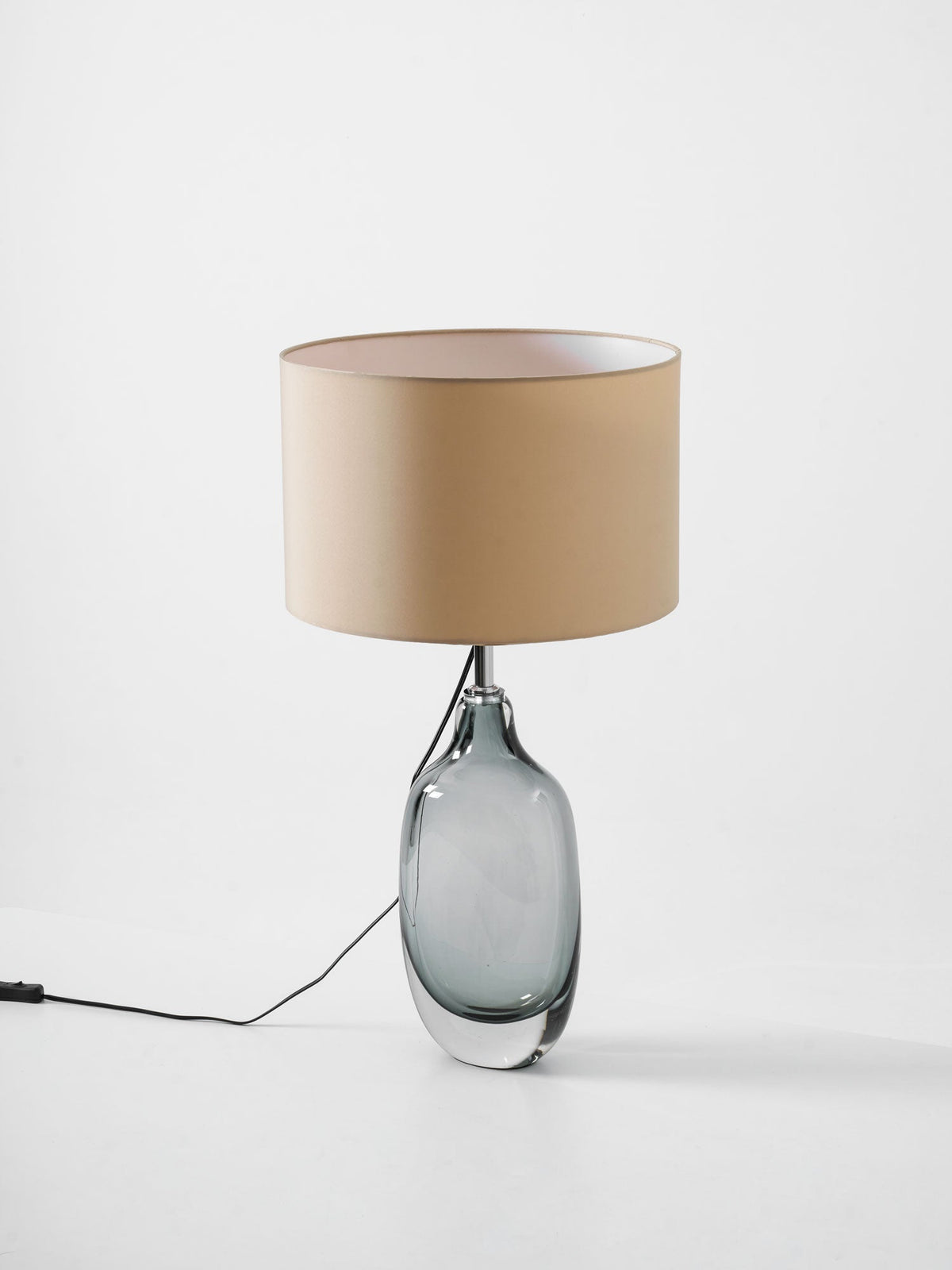 A three-quarter angle on the unlit Clérachic table lamp, showing its smoky glass base and cream shade on a pale grey backdrop.