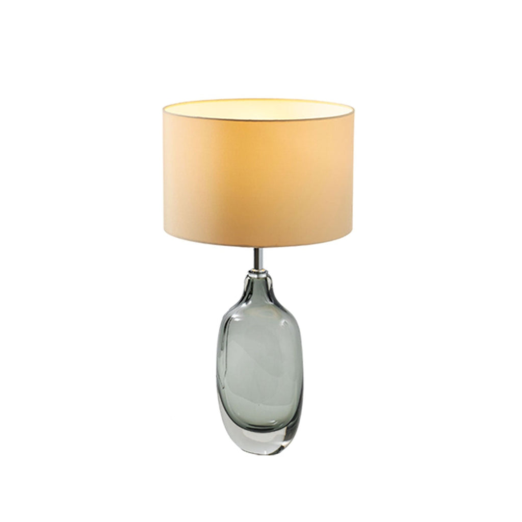 A Clérachic table lamp with a glowing cream shade and a smoky glass base on white, shown at a three-quarter angle.