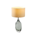 A Clérachic table lamp with a glowing cream shade and a smoky glass base on white, shown at a three-quarter angle.
