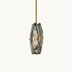 A faceted smoky grey crystal pendant from Clérachic on a brass rod, with brass pins holding two cut panels around a filament bulb, on white.
