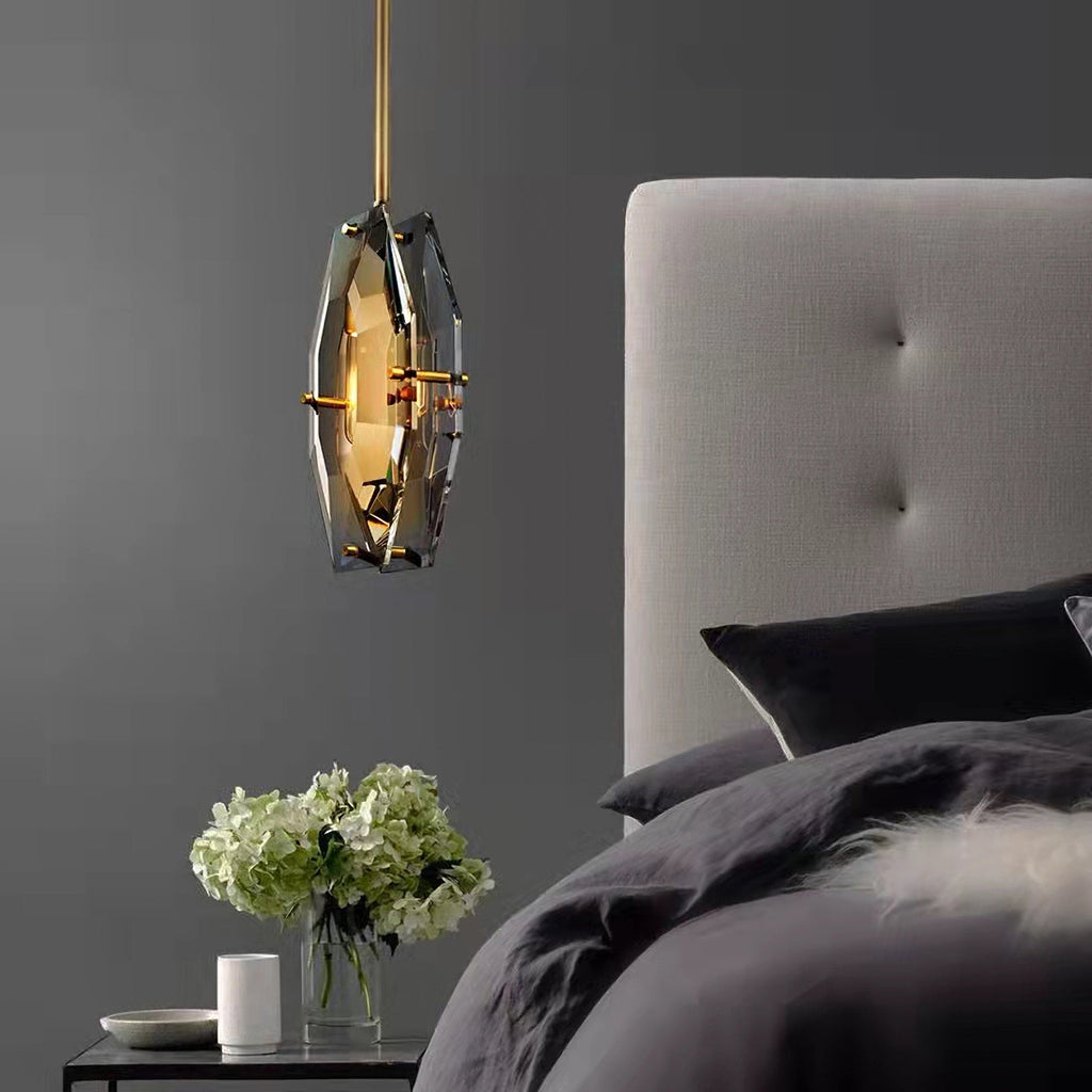 Smoky grey faceted pendant from Clérachic hanging beside a bed with a grey tufted headboard, dark bedding and a vase of white hydrangeas.