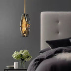 Smoky grey faceted pendant from Clérachic hanging beside a bed with a grey tufted headboard, dark bedding and a vase of white hydrangeas.