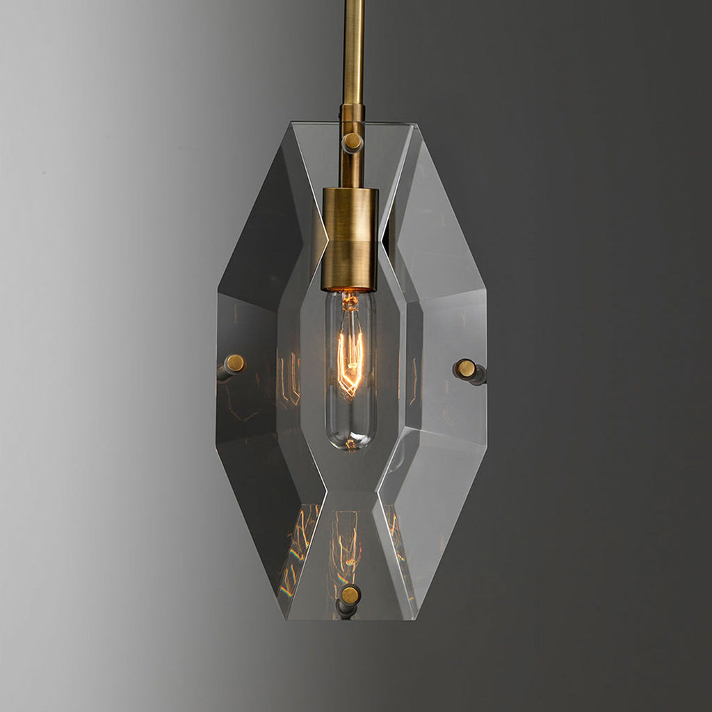 Front view of the cut crystal panel on this Clérachic pendant, with a brass bulb holder and a warm filament bulb glowing inside.