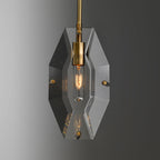Front view of the cut crystal panel on this Clérachic pendant, with a brass bulb holder and a warm filament bulb glowing inside.
