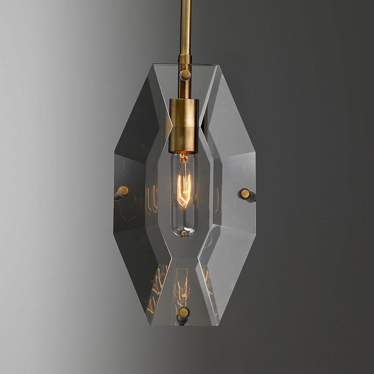Front view of the cut crystal panel on this Clérachic pendant, with a brass bulb holder and a warm filament bulb glowing inside.