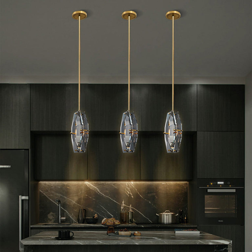 Three Clérachic crystal pendants hanging at one height on brass rods above a dark kitchen island, with a marble splashback behind.