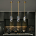 Three Clérachic crystal pendants hanging at one height on brass rods above a dark kitchen island, with a marble splashback behind.