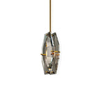 Clérachic faceted crystal pendant on a brass rod, set off-centre on a plain white backdrop with its brass pins visible.