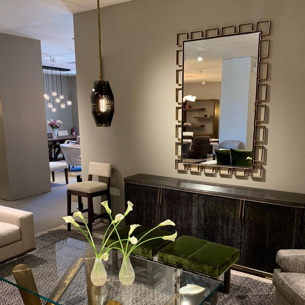A single dark smoky pendant from Clérachic hanging in a showroom beside a framed mirror, a low dark cabinet and a glass table with lilies.