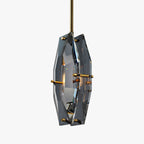 This Clérachic pendant on a light grey backdrop, with its grey-blue cut crystal panels and brass pins seen from a slight angle.