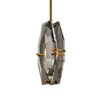 Clérachic crystal pendant on white from a three-quarter angle, with warm light inside the panels and brass pins at each edge.