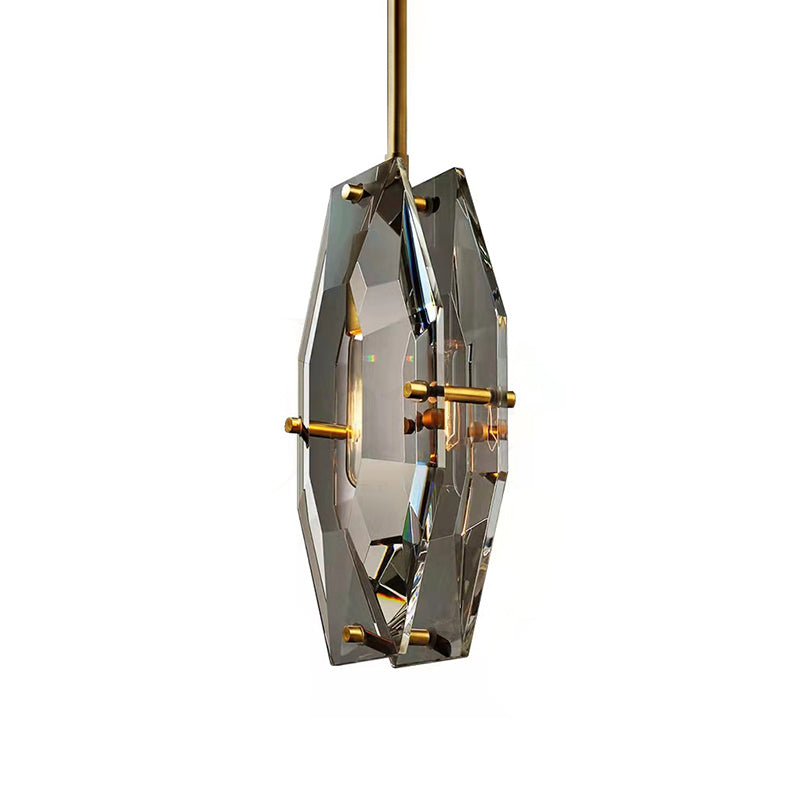 Clérachic crystal pendant on white from a three-quarter angle, with warm light inside the panels and brass pins at each edge.