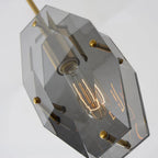 Looking up at the filament bulb inside this Clérachic pendant, with smoky grey panels, brass pins and the brass rod at an angle.