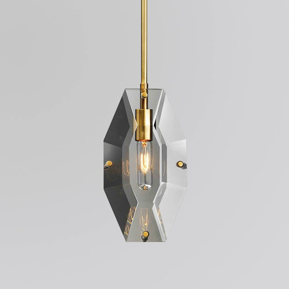 A Clérachic smoky grey crystal pendant on a brass rod, lit on a pale grey backdrop, with a hexagonal panel and visible filament.
