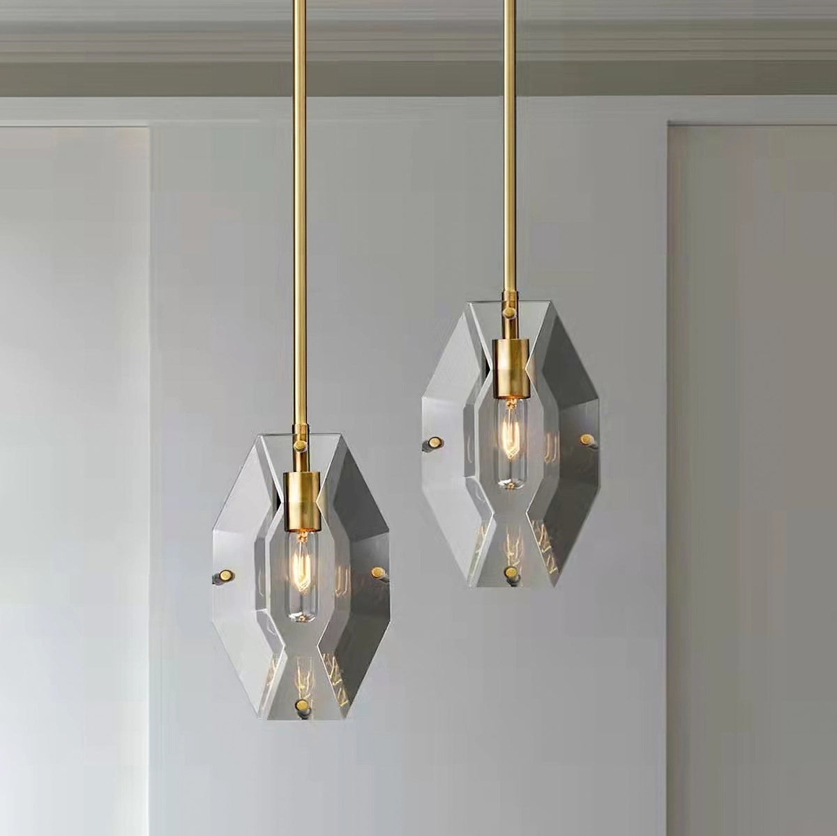Two Clérachic crystal pendants at different heights against a pale wall and panelled door, each with a brass holder and filament bulb.