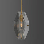 Front view of this Clérachic pendant on a mid-grey backdrop, with a hexagonal crystal panel and a brass holder around a lit bulb.