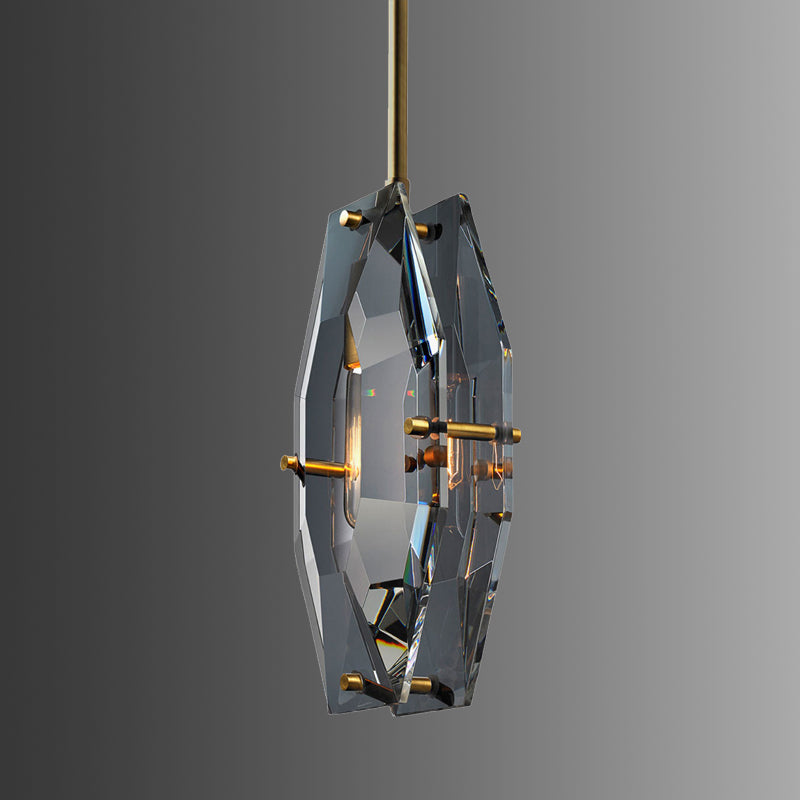 Clérachic crystal pendant angled on a grey gradient backdrop, with its brass pins and warm bulb glow seen through the cut glass.