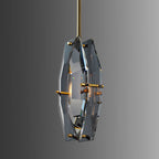 Clérachic crystal pendant angled on a grey gradient backdrop, with its brass pins and warm bulb glow seen through the cut glass.