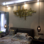 A Clérachic crystal pendant hanging beside a bed in a lit bedroom with a gold wall sculpture and a floral bedspread.