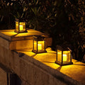 Clérachic black solar lanterns with flickering candle bulbs, glowing amber along a stone garden wall at night.