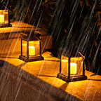 Clérachic black solar lanterns glowing amber on a stone wall in heavy rain, their glass sides keeping the candle bulbs lit.