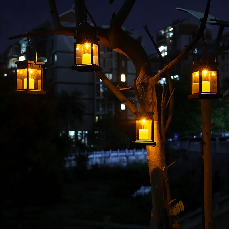 Four Clérachic black solar lanterns hung from tree branches and a post by their handles, glowing amber after dark.