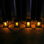 Four Clérachic black solar lanterns in a row on a wooden deck at night, each with a warm candle-style glow.