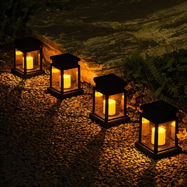 Four Clérachic black solar lanterns set along a gravel garden path, each lit with a warm candle-style flame.