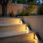Three Clérachic grey solar step lights glowing warmly along stone stair edges beside a gravel garden at dusk.