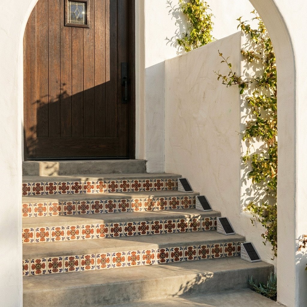 Four Clérachic grey solar step lights set along Talavera-tiled stair risers beside a carved wooden door.