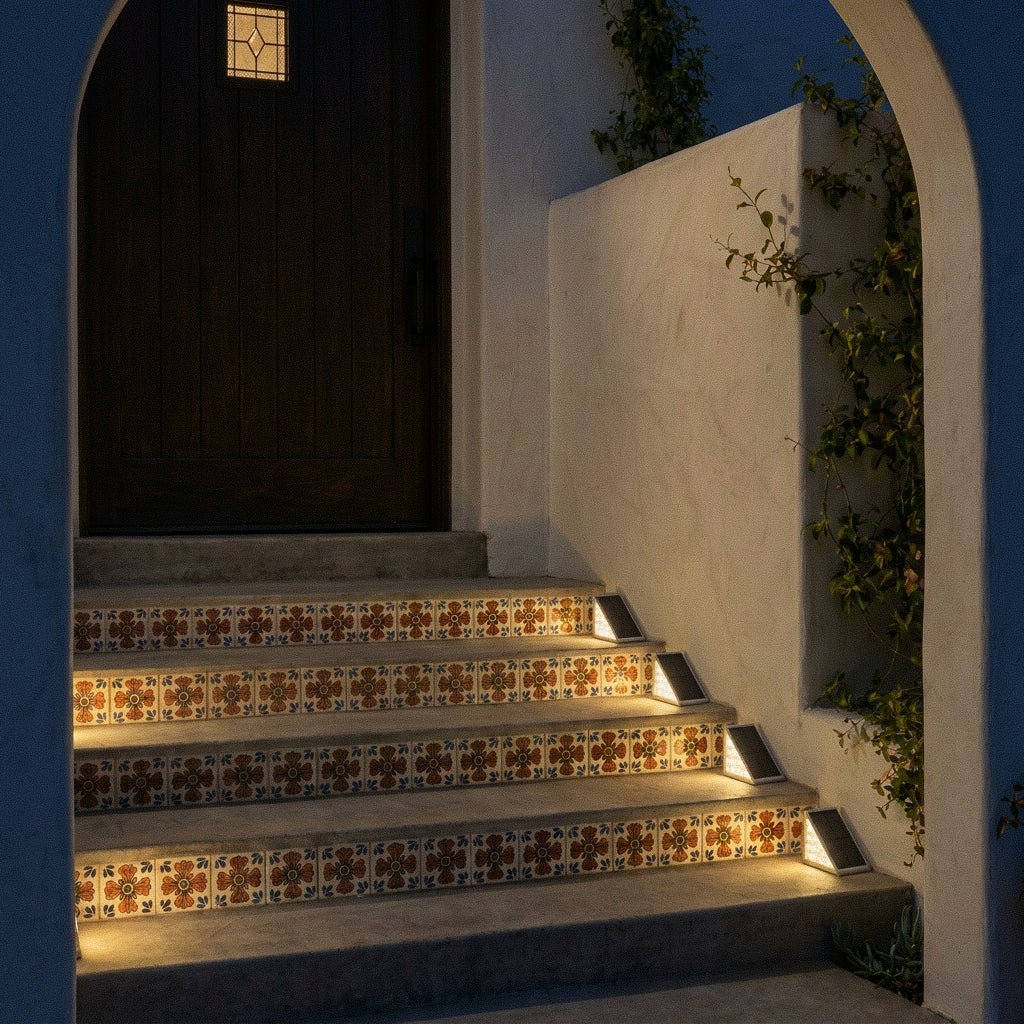 Four Clérachic grey solar step lights glowing warmly along Talavera-tiled stairs leading to a wooden door at night.