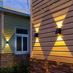 Clérachic black solar wall lamps on cedar-style cladding beside a window, throwing warm triangular beams up and down at dusk.