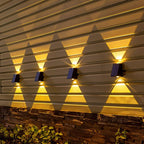 Four Clérachic black solar wall lamps in a row on horizontal siding above a stone base, each throwing warm up and down beams.