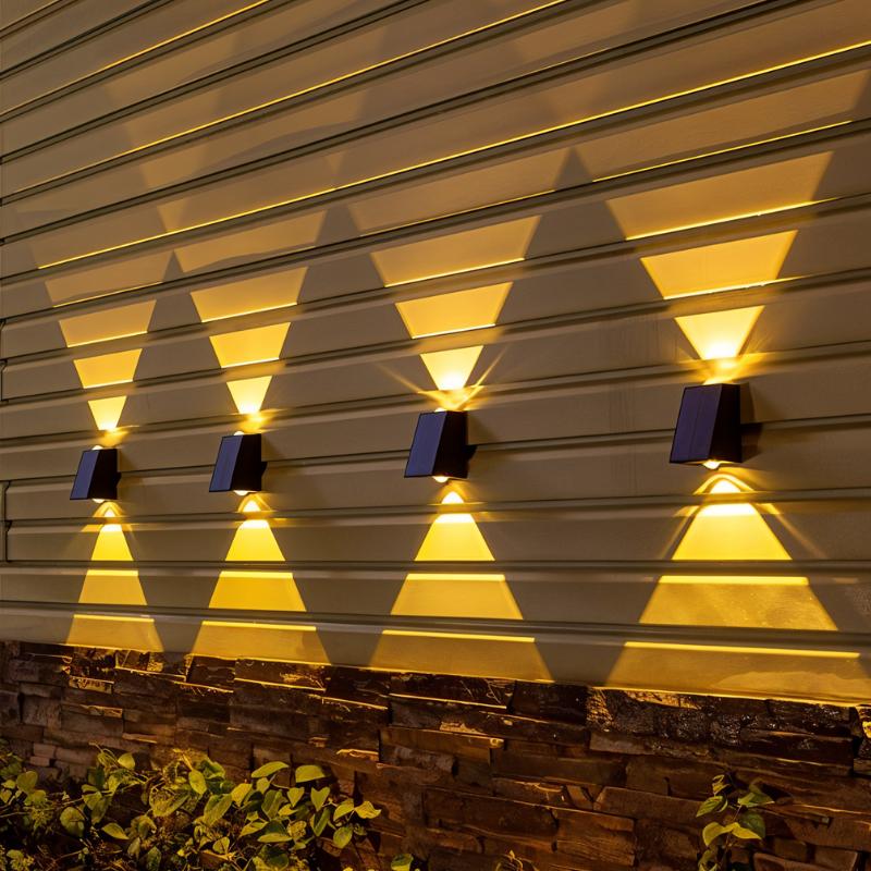 Four Clérachic black solar wall lamps in a row on horizontal siding above a stone base, each throwing warm up and down beams.