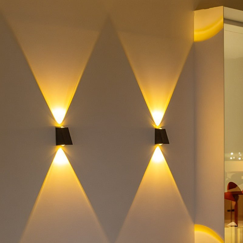 Two Clérachic black wedge wall lamps on a cream wall, each casting a warm cone of light upward and downward in the evening.