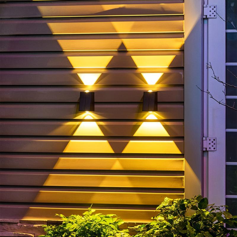 Clérachic pair of black solar wall lamps on dark siding beside a white door frame, glowing warm up and down among green leaves.