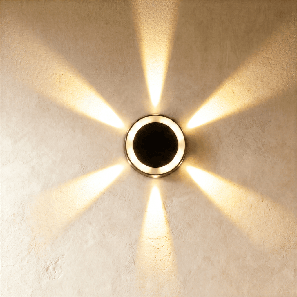 Clérachic small round solar wall light glowing warm white, throwing a six-way star of light across limewash plaster.