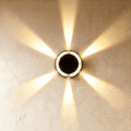 Clérachic small round solar wall light glowing warm white, throwing a six-way star of light across limewash plaster.