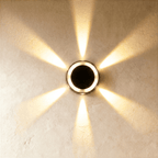 Clérachic small round solar wall light glowing warm white, throwing a six-way star of light across limewash plaster.